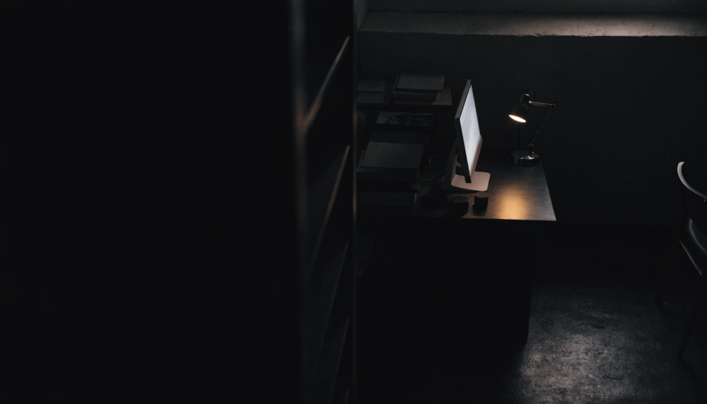 Late-night workspace with laptop and notebook, illuminated by soft desk lamp glow, suggesting hours of creative work and contemplation.